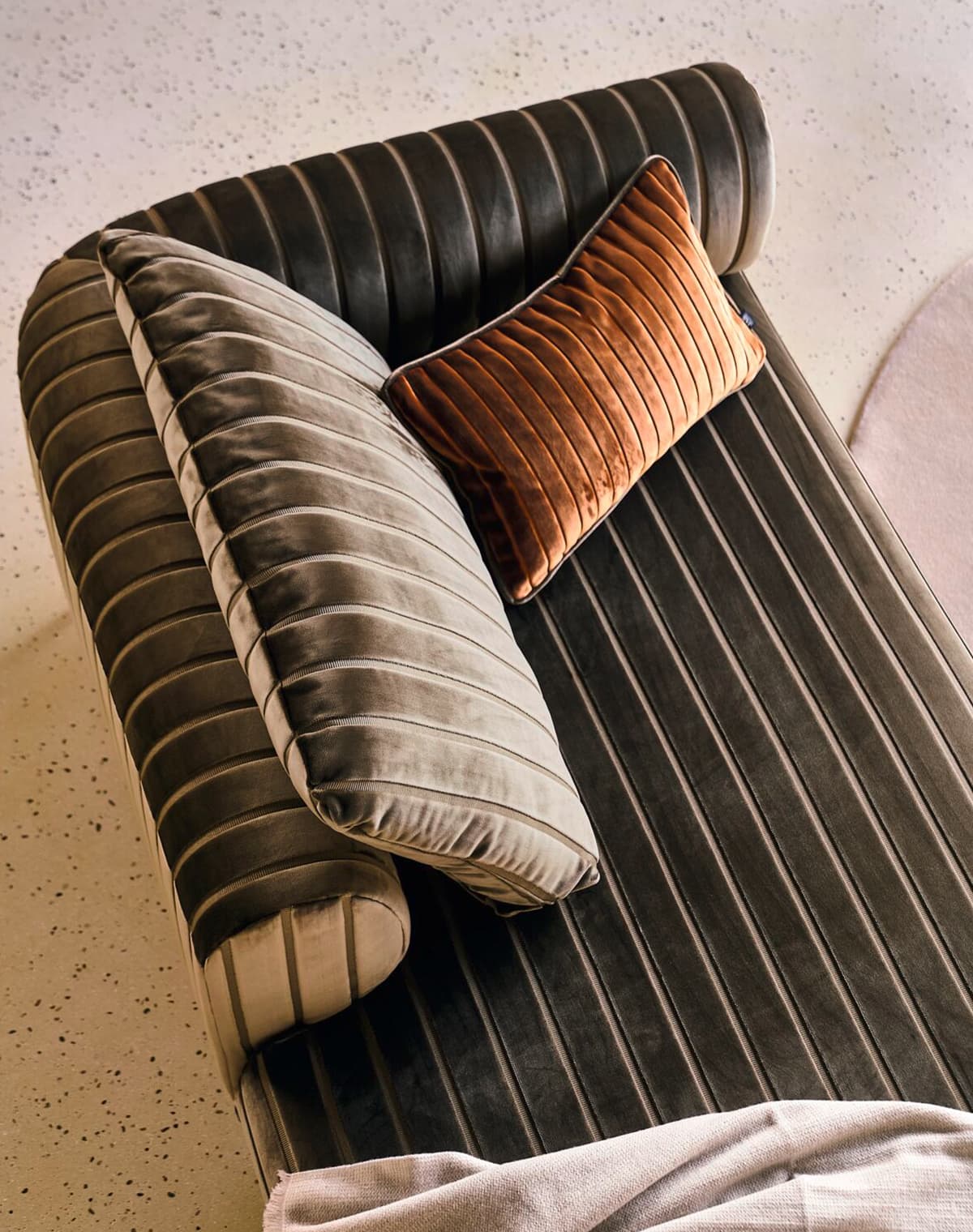 Eine Aufnahme von einem Sofa, bezogen in bronze, mit zwei Kissen darauf. 