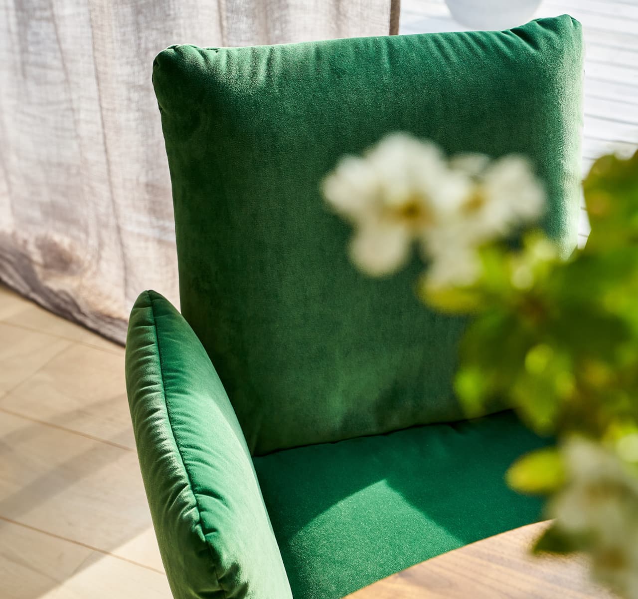 Detailbild von einem Esszimmerstuhl mit grünem Polster. Im Vordergrund ist eine Blume zu sehen.