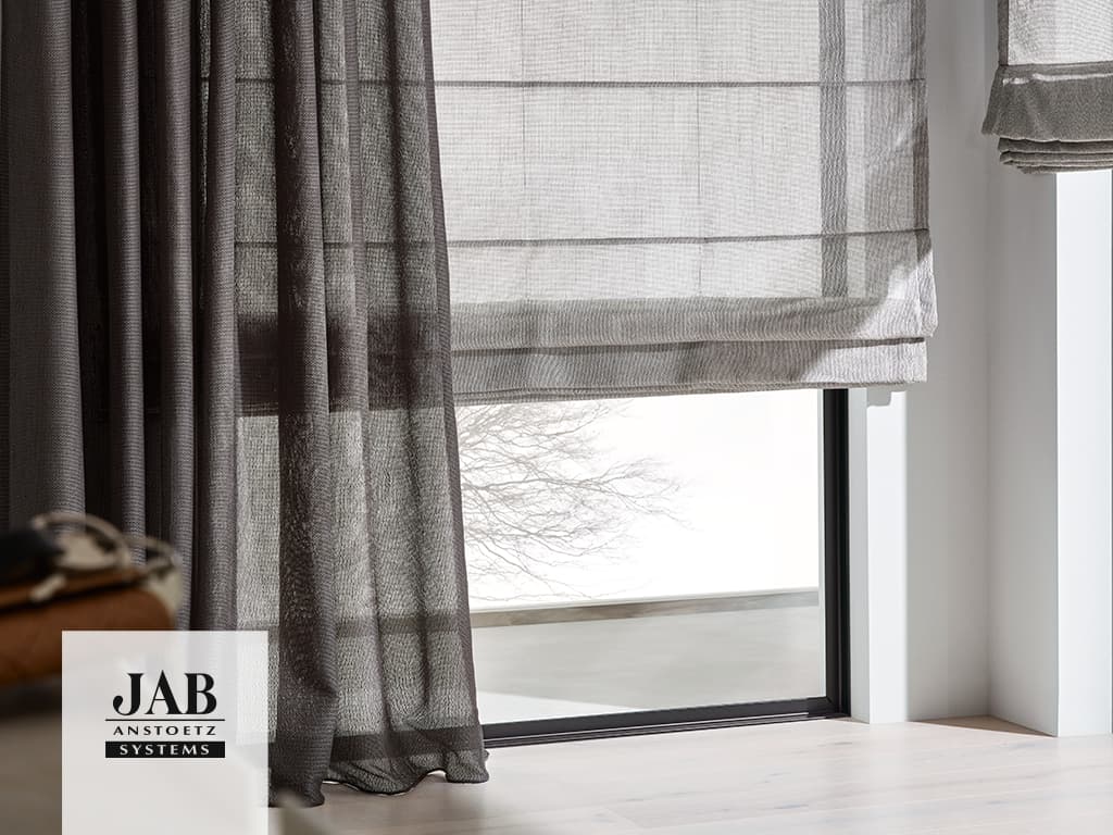 Hellgraues Faltrollo und dunkelgrauer Vorhang an einem Fenster mit schwarzem Rahmen.