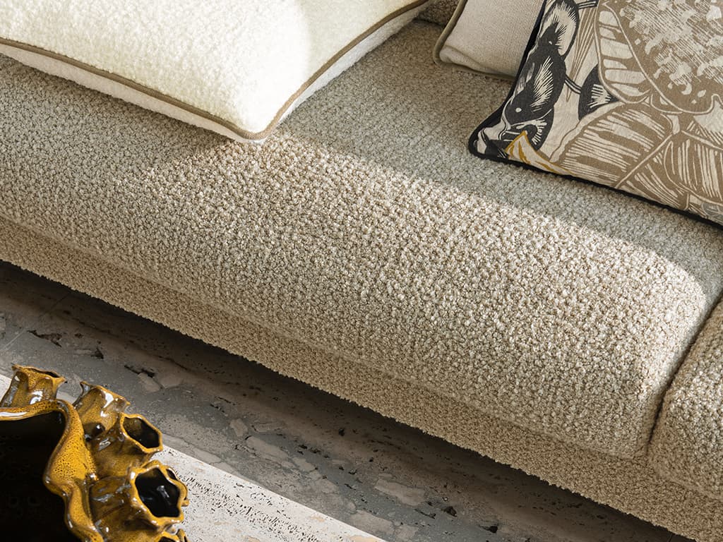 Das Bild zeigt eine Detailaufnahme eines weißen Sofas mit verschiedenfarbigen und gemusterten Kissen. Der Steinboden mit unterschiedlichen Kontrasten betont die Strukturen der Stoffe wunderbar.