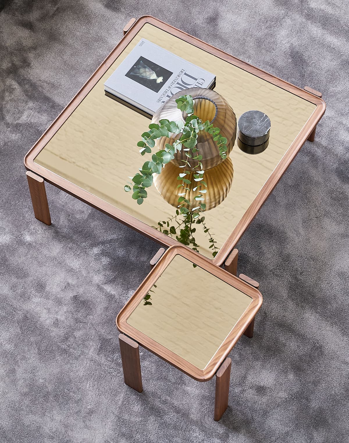 Zwei Holz-Couchtische mit Glasplatten aus der Vogelperspektive auf einem grauen Teppich