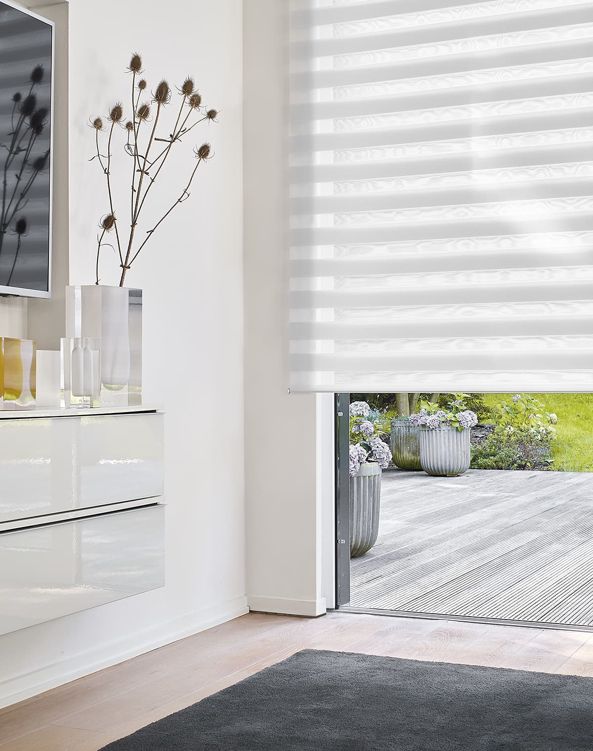 Flur mit einem weißen Sideboard an der Wand und bodentiefem Fenster mit einem weiß gestreiften Doppelrollo