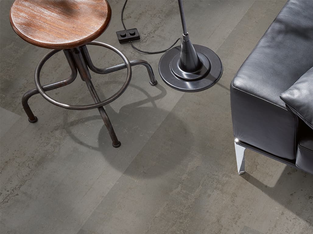 Grauer LVT in Steinoptik darauf steht ein Hocker, eine Lampe und ein Sessel