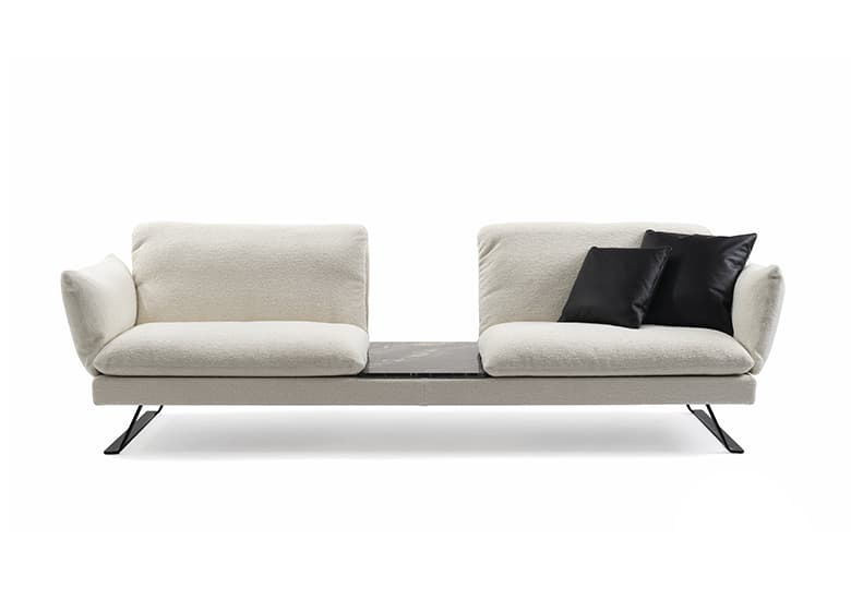 Freisteller eines weißen Sofas mit einem angebauten Tisch zwischen den beiden Sitzelementen. Auf dem Sofa liegen zwei schwarze Deko-Kissen.