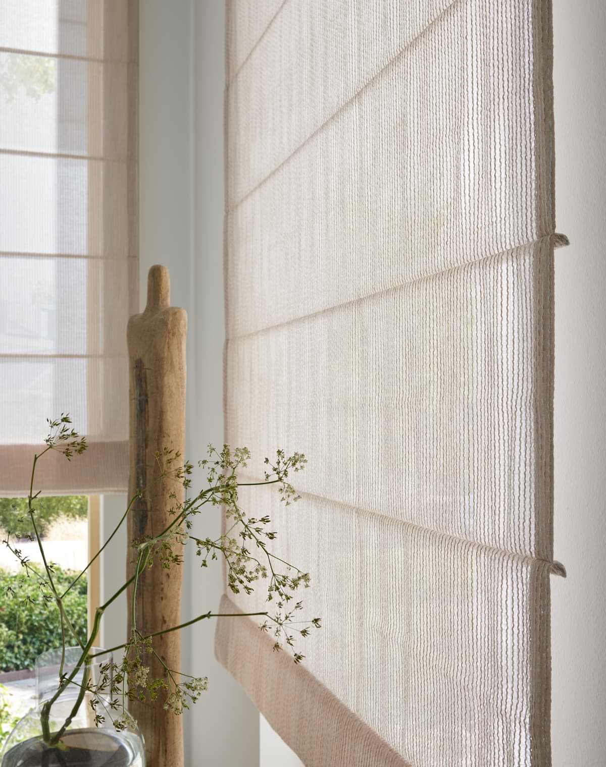 Nahaufnahme des Faltrollos Cozy Line in beige mit verschwommenen Blätter davor