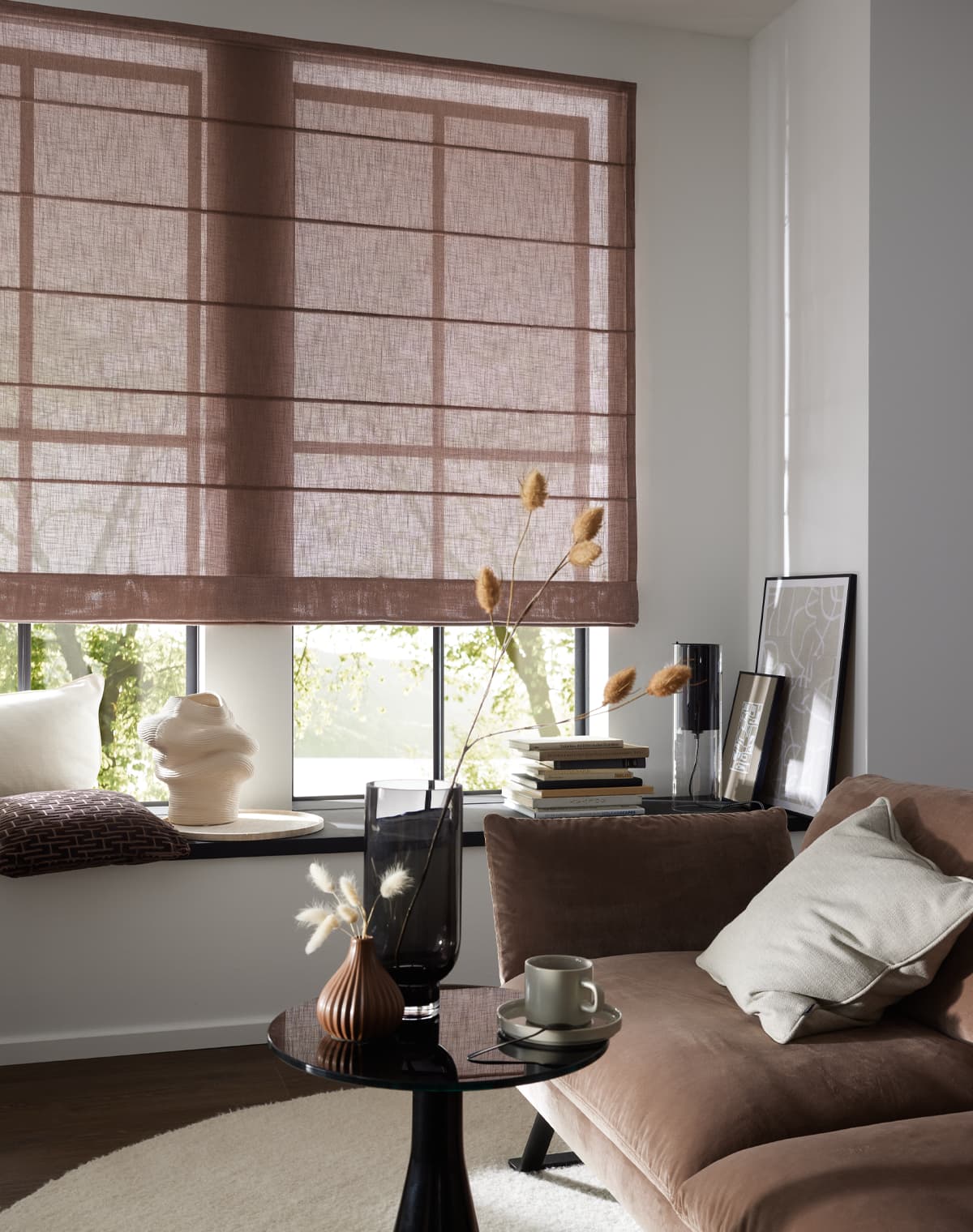 Faltrollo Sandy Island in altrosa an einem Fenster vor welchem die Fensterbank als Sitzbank dient, davor steht ein rose-farbenes Sofa auf einem weißen Teppich, welcher auf dunklem Holzboden liegt
