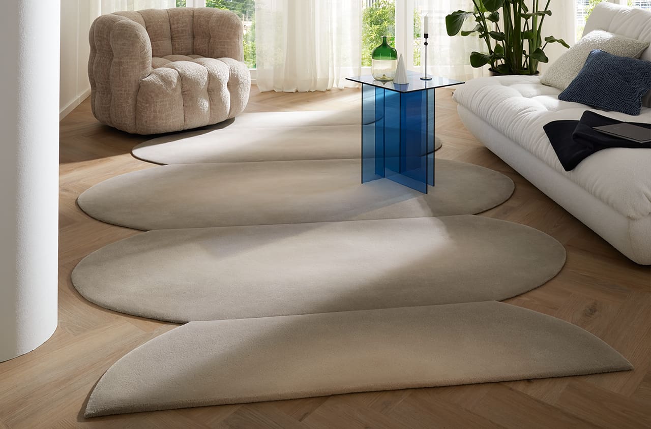 Teppich Barocca in beige in eienr Raumsituation mit einem weißem Sofa, beigen Sessel udn blauen kleinen Tisch sowie einer Pflanze und Lampe