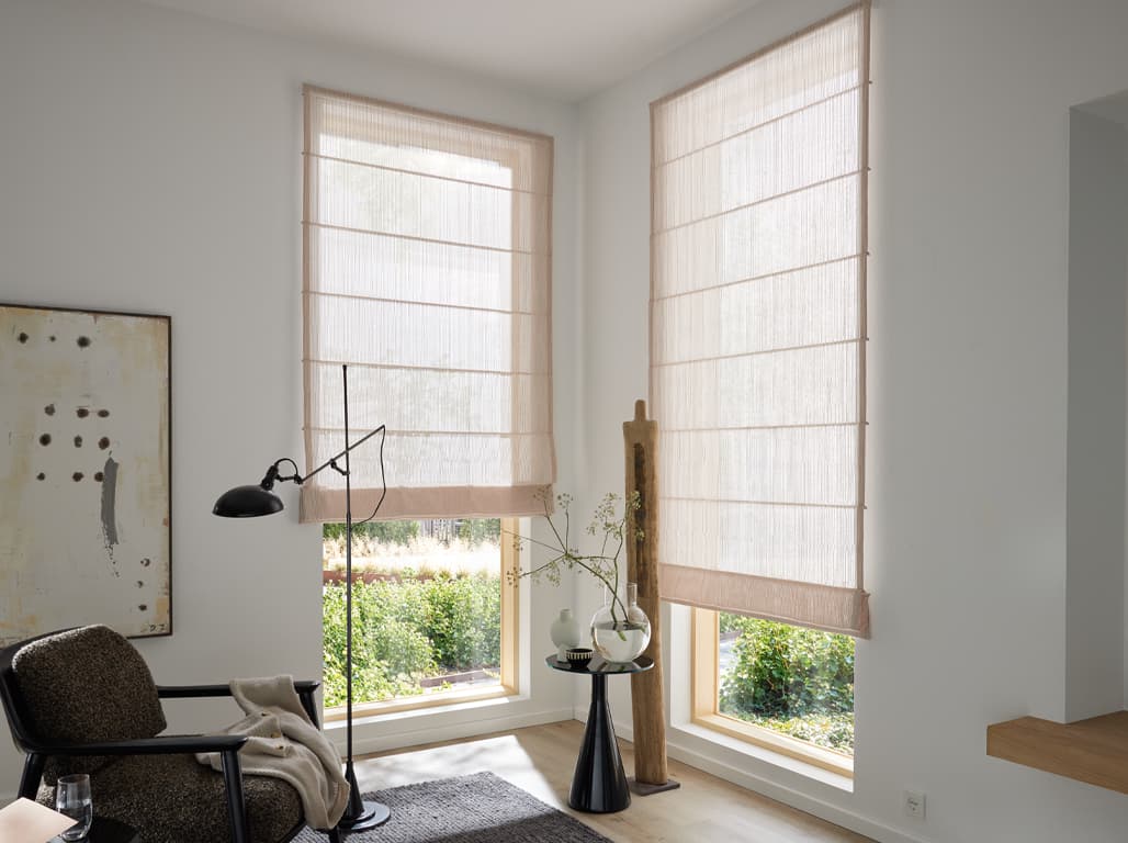 Faltrollo Cozy Line in einer Raumsituation mit einem schwarz-braunen Sessel auf der linken Seite, einem beige-braunen Bild an der Wand und Holzboden