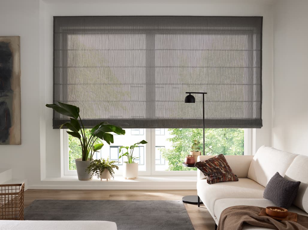 Faltrollo Charming Stripe in grau in einer Wohnsituation mit weißem Sofa, schwarzer Stehlampe, Blumen und einem grauen Teppich auf Holzboden