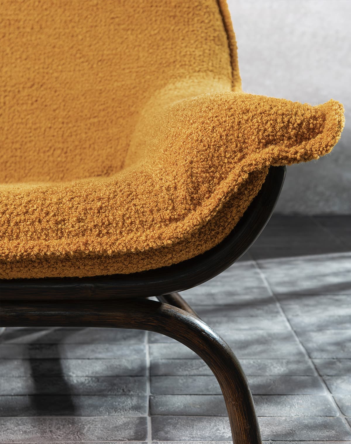 Das Bild zeigt eine Detailaufnahme eines orangefarbenen Sessels. Die Kontraste und Strukturen des Stoffes kommen gut zur Geltung. Das Holzgestell des Sessels harmoniert farblich mit den Kontrasten des orangefarbenen Stoffes.