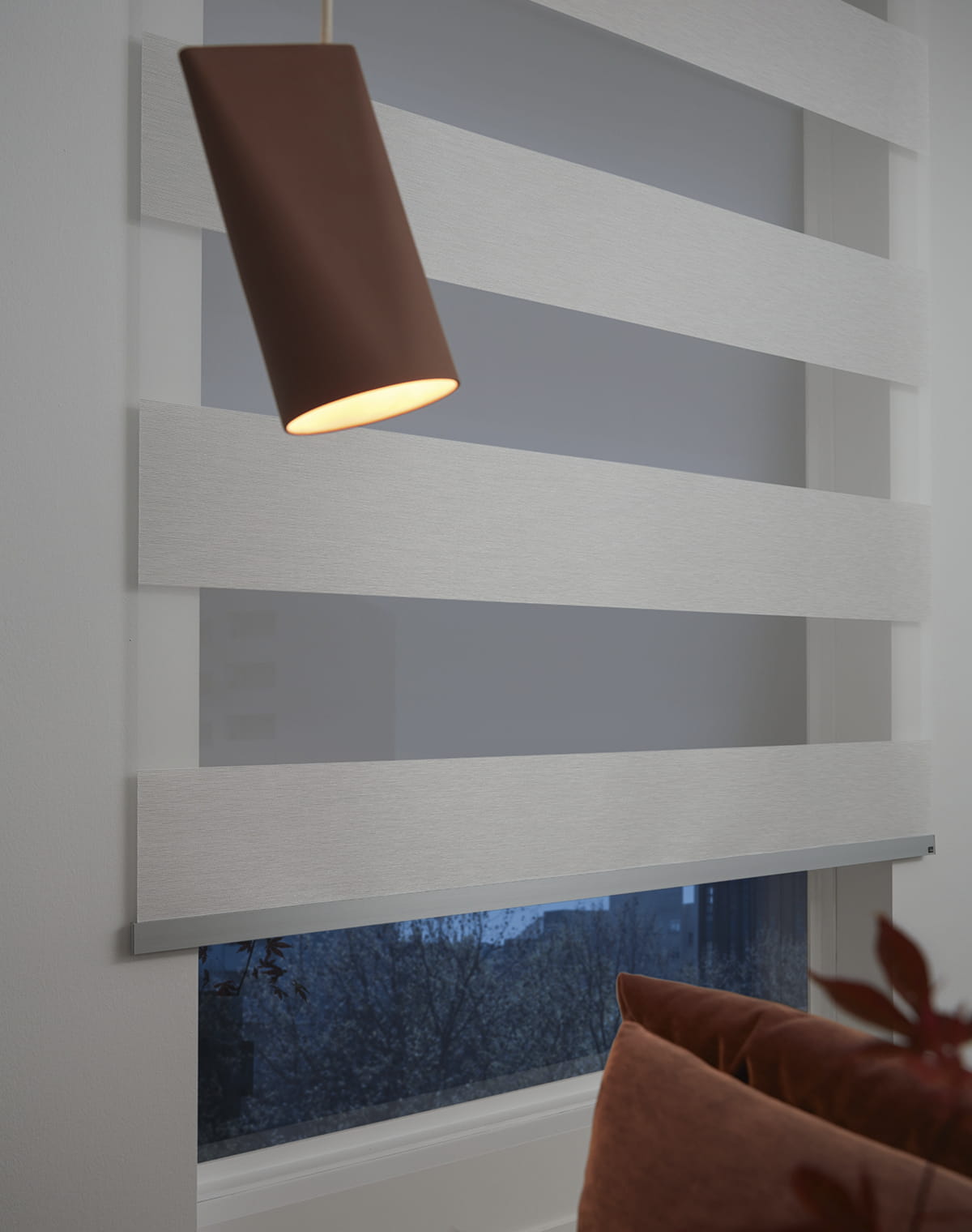 Rostbraunes Sofa vor einem Fenster mit weiß gestreiftem Rollo