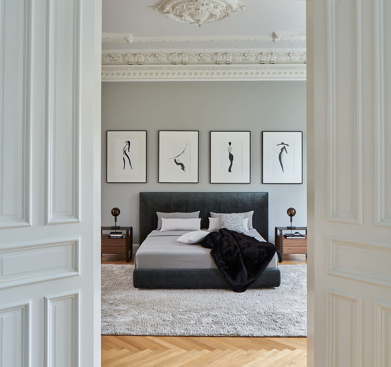 Blick durch eine geöffnete Altbau-Tür, in ein Schlafzimmer auf ein graues Polsterbett.