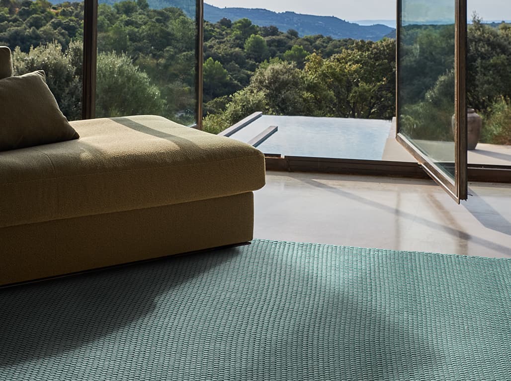 Grüner Teppich vor der offenen Terrassentür unter einem grünen Sofa