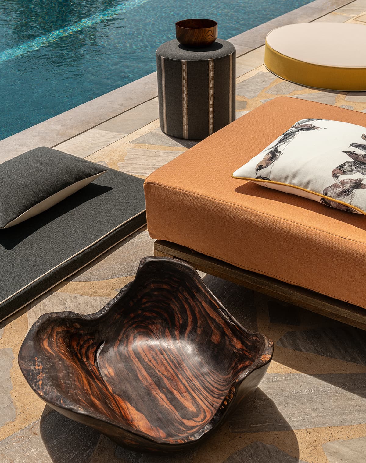 Eine Feuerschale, eine orangene Liege, ein schwarzes Kissen und ein schwarzer Pouf am Pool.