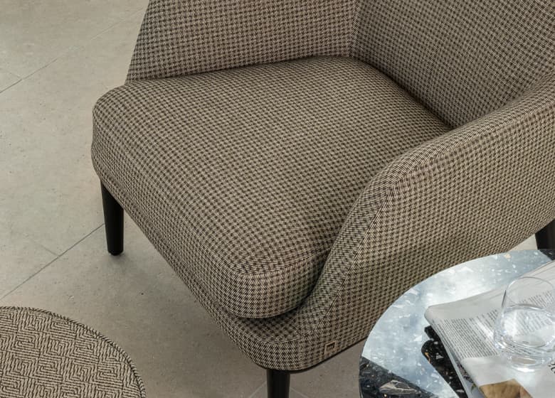 Multiprotect Stoff Allrounder in beige auf einem Sessel und Hocker, neben welchen ein kleiner Tisch steht