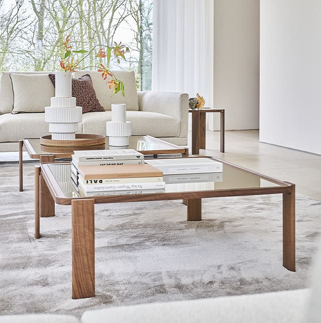 Zwei Holz-Couchtische mit Glasplatten in einem hellen weißen Raum